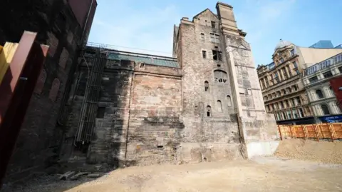 PA Media Historic stone building overlooking a cleared construction site.