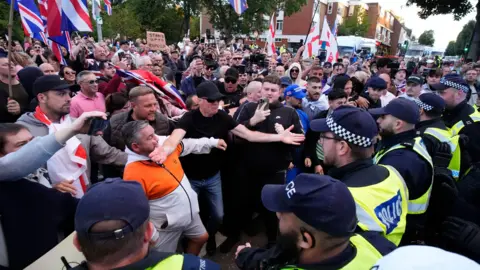 PA A large crowd of demonstrators, some of whom are waving flags and signs, get close to a line of police officers during a protest march.