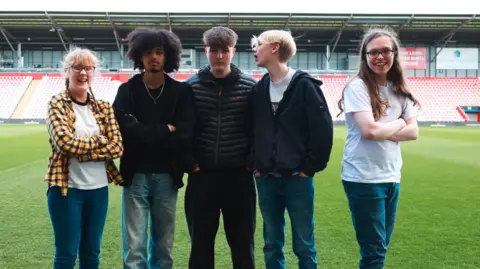 Deacon Communications Five young people stand on a sports field and poses for a music video
