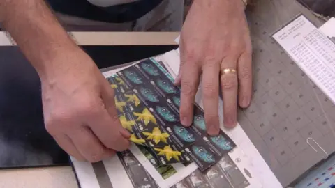 Two hands tearing postage stamps out of a folder