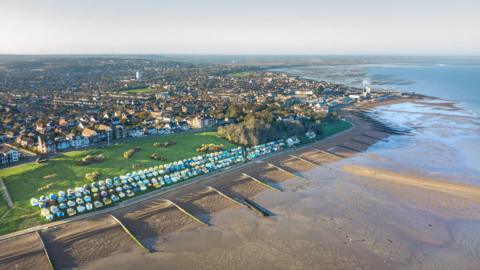 An aerial photograph of the Whitstable coastline showing houses and groynes along a pebbly beach