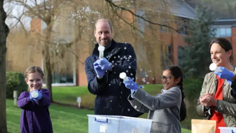 The Prince of Wales with local schoolchildren as they filter DNA samples through a syringe after extracting water from a local pond in order to see which species live in it