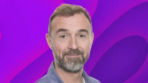 A headshot of Brenner Woolley. He has short light hair and a light beard with some grey in it. He wears a grey shirt. There is a purple background behind him.