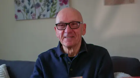 Paul Perkins. Paul is sitting down, bald and has glasses.