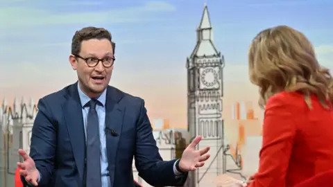 BBC Chief Secretary to the Treasury Darren Jones appearing on Sunday with Laura Kuenssberg. He wears a navy suit, a pale blue shirt and a navy tie. 