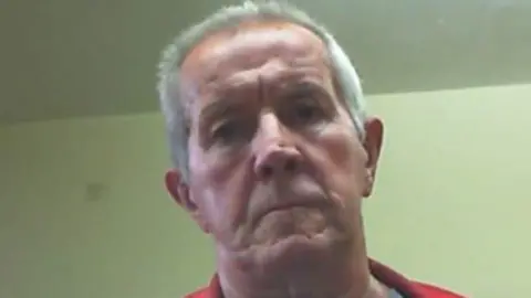 Avon and Somerset Police Richard Scatchard is wearing a red jacket and is looking down at the camera.