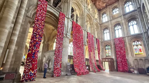 Peterborough Cathedral Long panels of crocheted and knitted poppies, mostly red or white, hanging from the arches of Peterborough Cathedral.