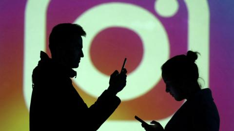 Silhouette of two people using their smartphones with Instagram's logo in the background