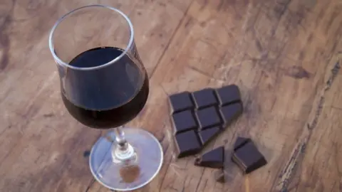 Getty Images A glass half full of red wine on a table, beside half-eaten dark chocolate.