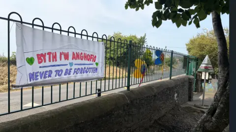 A school fence with a banner which reads: Never to be Forgotten - Byth i'w Anghofio