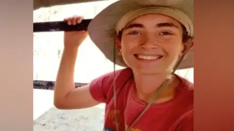 A young boy on holiday. He is smiling and wearing a big hat. 
