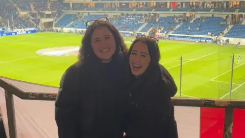 Emma de Duve Emma smiling inside a football ground with another woman