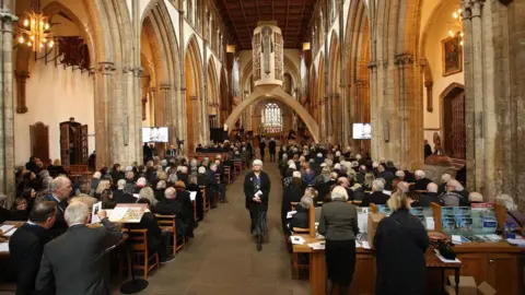 Athena Picture Agency The inside of a cathedral, looking from the back of the church, with all the seats filled with people dressed in black