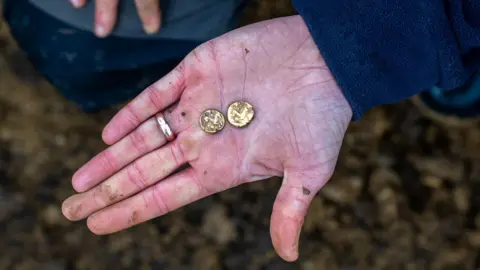 Two small gold coins laid in the palm of someone's hand.