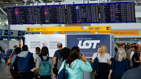 AFP via Getty Images Passengers check their delayed flights on monitors at the international airport in Warsaw
