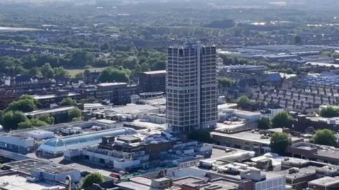 A large office block and trees and houses from an aerial view.