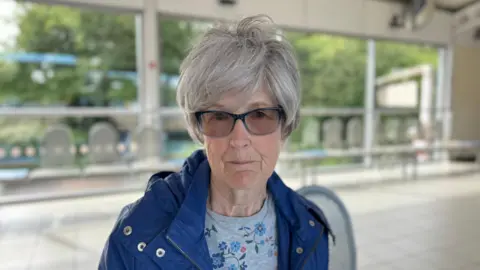 George King/BBC Carol Smith in a blue coat, wearing glasses