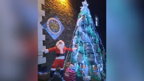 Santa stands outside The Griffin Inn with its 4m high  illuminated Christmas Tree made out of beer barrels