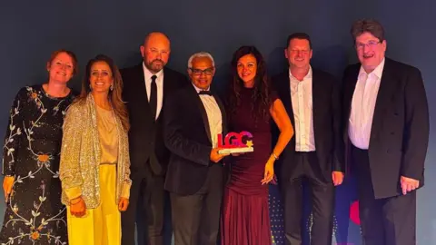Bradford Homeless Outreach Partnership The Homeless Outreach Partnership team with their award: three women in dresses and four men in suits standing in a group holding an award
