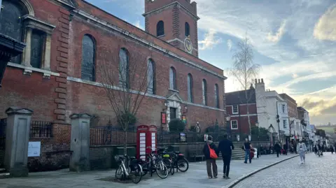 Strettons A red telephone box in front of a church on a cobbled street.