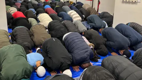 Jon Wright/BBC A room full of people kneeling on the floor with their heads bowed down in prayer