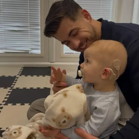 Morgan Deakin A man holding a baby wearing blue and holding a blanket with teddy bears on it