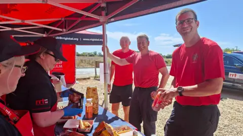 Rapid Relief Team A group of firemen in red T-shirts, collecting food from volunteers inside a red and black tent.