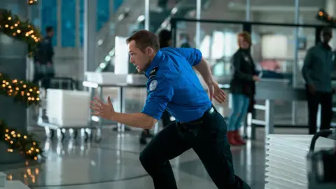 Netflix Taron Egerton as TSA agent Ethan Kopek, running through LAX.