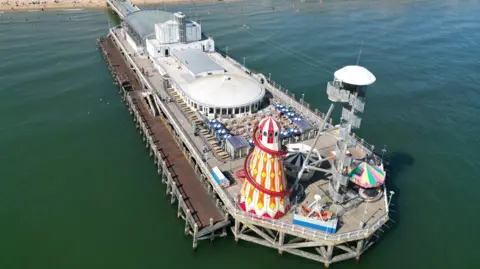 Red, white and orange helter skelter and other fairground rides on the end of a pier