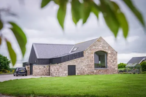 The opposite end of the house is in a blonde stone with another large window, this one with an arched top.