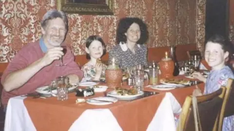 Press Association/Kent Police A dinner table with orange table cloth and candles and plates of food. A grey-haired man, brunette woman and two young brunette girls are sat around the table. They are smiling and looking at the camera.