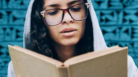 A woman with glasses and a hoodie reads a book