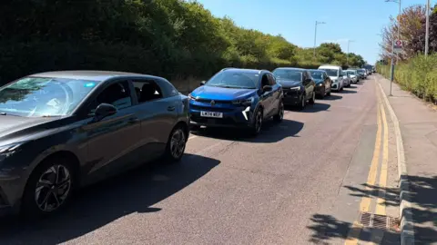 Daytime traffic jam on a road, showing a long queue of cars and a white van