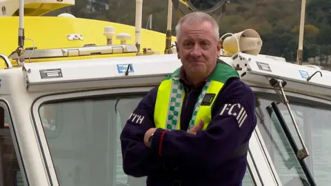 Man in a Guernsey stood near the bow of a boat