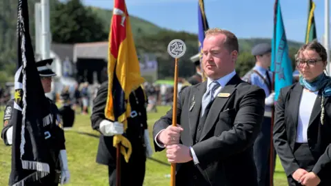A member of staff of the Office of the Clerk of Tynwald carrying an official staff in the procession.