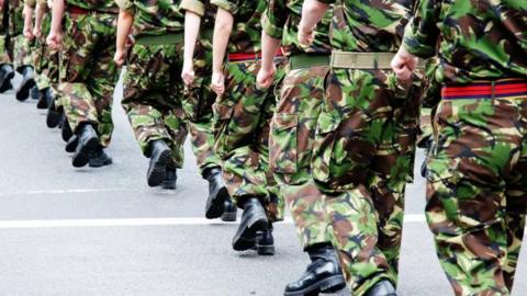 People dressed in camouflage military uniforms marching in a lines