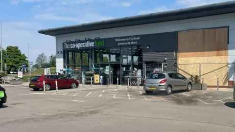 John Devine/BBC Frontage of the Co-op store with some cars parked in front. A large section has been boarded up. 