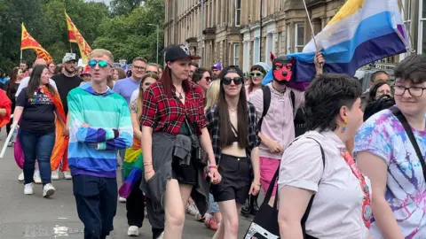 Pride marchers in Glasgow carrying flags and wearing colourful clothes  
