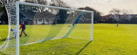 Poets' Corner FC Goalposts on a football pitch with two children and an adult in the background.