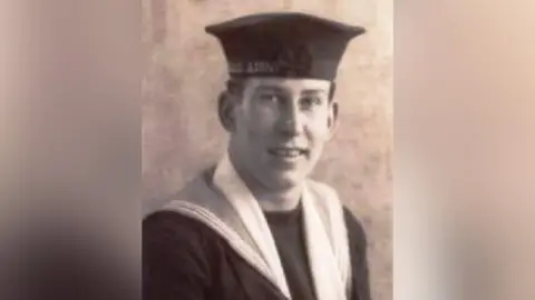 Tony Winter A young George Winter in a black and white headshot style image. He is wearing sailors uniform, including a hat.