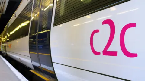 The side of a c2c train. The picture has been taken close to platform level and the train is white with a pink c2c logo on the side of it.