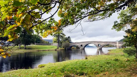 A view of Kenmore Bridge at the opening to Loch Tay which separates the lake from the river of the same name - as seen here from under autumnal trees.
