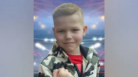 Family An eight-year-old boy in a cargo print jacket and red t-shirt against a CGI boxing arena background