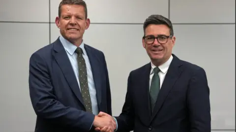 A formal picture of Rhun ap Iorwerth and Andy Burnham shaking hands