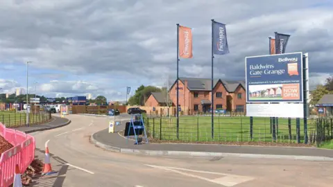 Google A Google street view image showing the entrance into a new housing development. A Bellway-branded blue sign on the right of the entrance says Baldwin's Gate Grange.