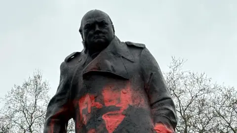 Black statue of Winston Churchill with red graffiti 