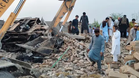 EPA People survey the scene as a digger moves rubble following a car bombing in Bannu, Pakistan.