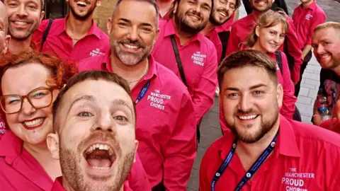 ManchesterProudChorus Members of the Manchester Proud Chorus choir pose for a photo wearing pink polo shirts emblazoned with the choir's name.