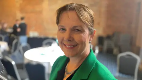 Mayor Claire Ward, looking at the camera while posing in front of a reception area