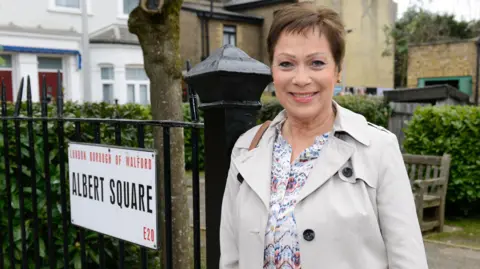Denise Welch pictured on EastEnders in 2016 next to an Albert Square sign